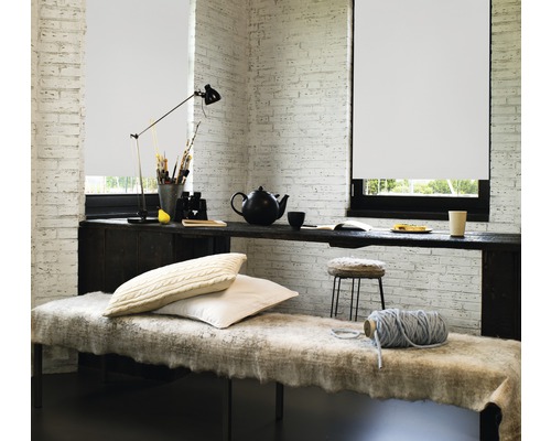 Lichte kamer met rolgordijn, bureau en zitgelegenheid.