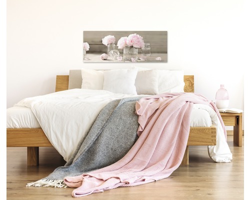 Slaapkamer met bed, dekens en een afbeelding van bloemen
