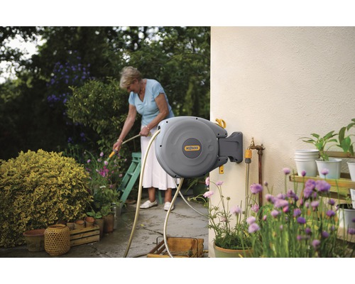 Automatische haspel aan een huisgevel met een vrouw die de tuin besproeit