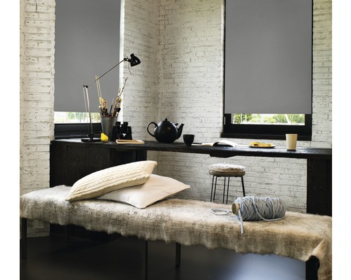 Decoratieve kamer met grijze rolgordijnen voor de ramen en een tafel met diverse objecten.