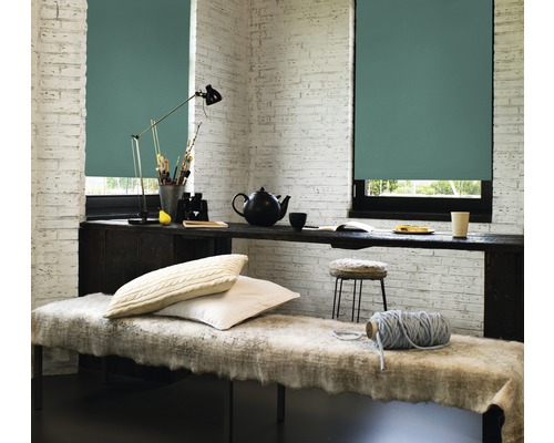 Lichte kamer met twee ramen voorzien van rolgordijnen, een bank en een bureau met decoratieve objecten