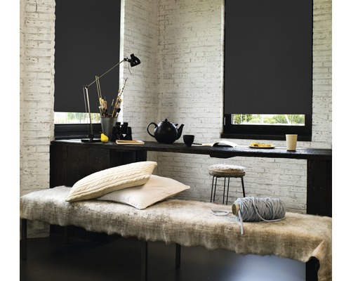 Kamer met zwarte rolgordijnen, tafel en zitbank voor een bakstenen muur