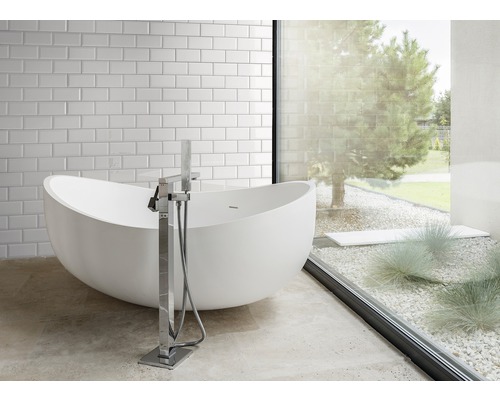 Badkamer met vrijstaand bad, kraan en raam met uitzicht op de tuin