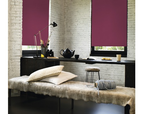 Woonkamer met twee ramen en bordeauxrode rolgordijnen, bureau en zitbank