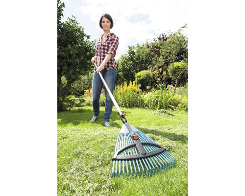 Een vrouw gebruikt een bladhark in de tuin om gras te harken.