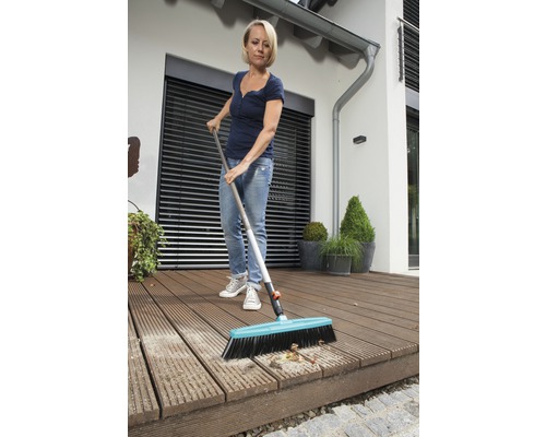 Vrouw maakt een houten terras schoon met een straatbezem.