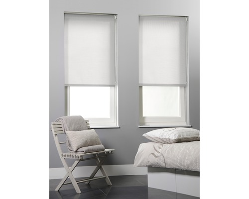 Twee witte rolgordijnen op ramen in een slaapkamer met een stoel en een bed