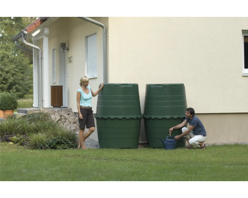Twee groene regentonnen in de tuin voor een huis, een man vult een gieter