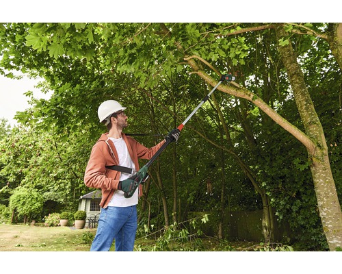 Man met veiligheidshelm snoeit takken met een stokzaag in de tuin.