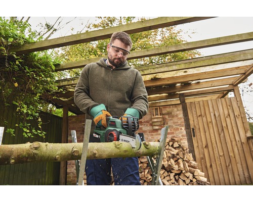 Man zaagt hout met een draadloze kettingzaag in de tuin