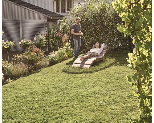 Vrouw ontspant op een tuinligstoel in de tuin, terwijl een man ernaast staat.