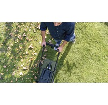 Persoon duwt grasmaaier over gazon met bladeren