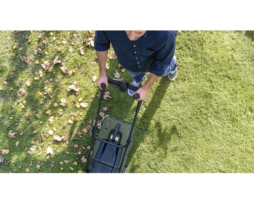 Persoon duwt grasmaaier over gazon met bladeren