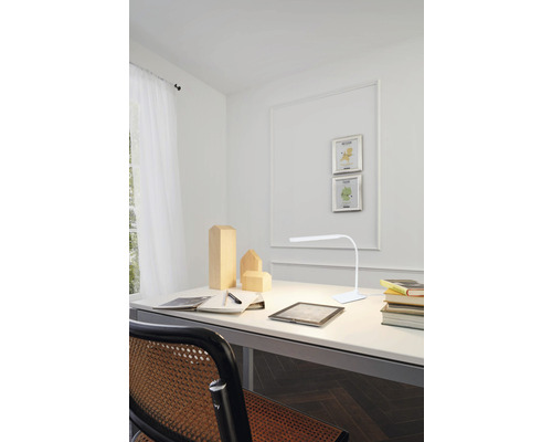 Bureau met lamp, notitieboek, pen en houten figuren in een heldere kamer.