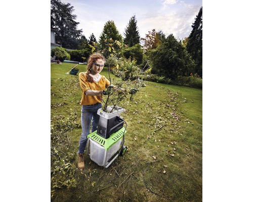 Vrouw gebruikt een elektrische hakselaar in de tuin om takken te versnipperen