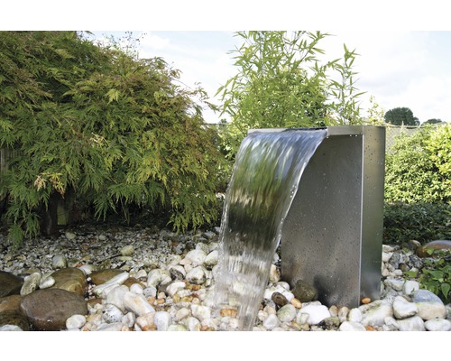 Tuinscene met een roestvrijstalen waterval, omgeven door stenen en planten.
