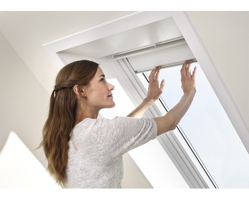 Een vrouw bedient een dakraam in een lichte kamer.