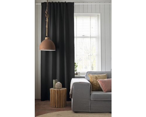 Woonkamer met bank, houten bijzettafel, lamp en zwart gordijn.