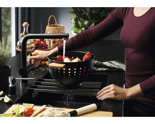 Spoelbak met afdruiprek, kraan en vrouw die groenten wast