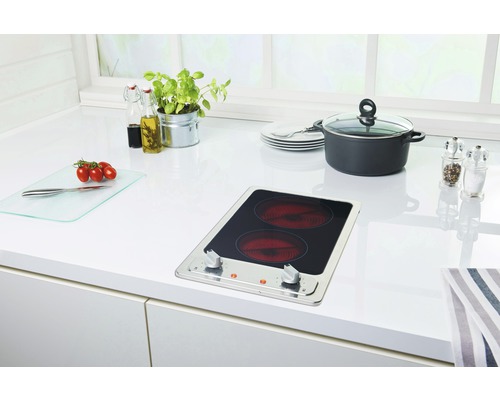 Keukenscène met kookplaat, pan, servies en voedsel op een wit aanrecht.