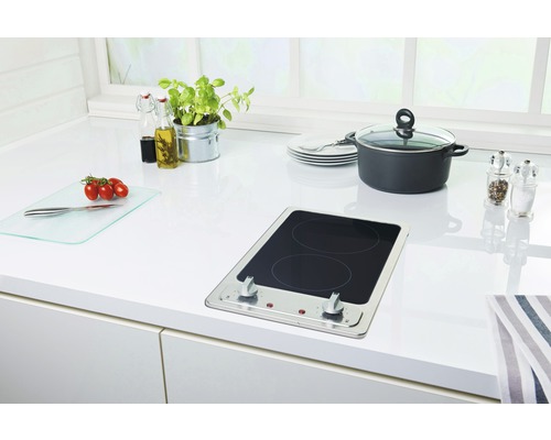 Keukenscène met kookplaat, pan, snijplank en keukengerei op een wit aanrecht.