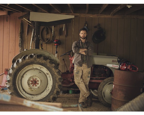 Man staat voor tractor en kettingzaag in een werkplaats