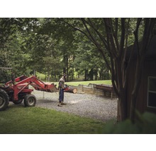 Man zaagt hout met een kettingzaag naast een tractor op een erf.