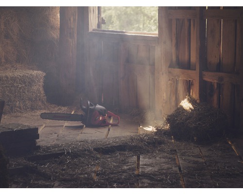 Scène in een schuur met een kettingzaag op de grond en hooibalen op de achtergrond.