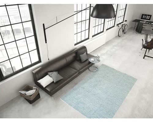 Lichte woonkamer met bank, vloerkleed met geometrisch patroon, lamp en ramen