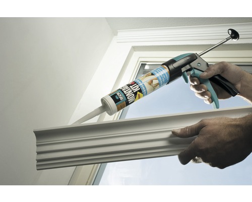 Een kitpistool met montagekit wordt gebruikt om een sierlijst aan een raamkozijn te bevestigen.