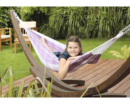 Meisje ontspant in een gestreepte hangmat met houten frame in de tuin