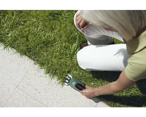 Vrouw knipt gras met een accugrasschaar langs een stenen pad