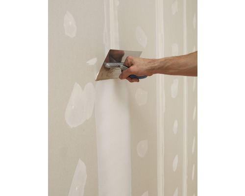 Een vakman plakt een gipsplaten muur met een plamuurmes.