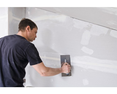 Een man egaliseert een gipsplatenwand met een plamuurmes