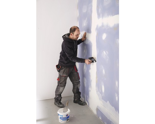 Man pleistert muur met vulmiddel en plamuurmes