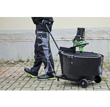 Persoon duwt mortelmachine op wielen over straatstenen.