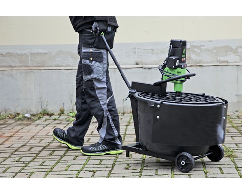Persoon duwt mortelmachine op wielen over straatstenen.
