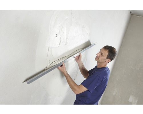 Man egaliseert gips op een muur met een pleisterspaan