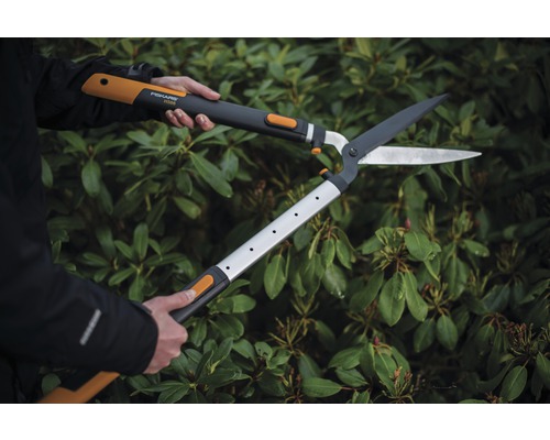 Een persoon gebruikt een heggenschaar met tandwieloverbrenging voor een groene heg.