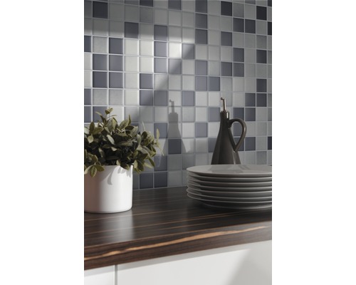 Mozaïektegelwand boven een donker aanrechtblad met servies en decoratie