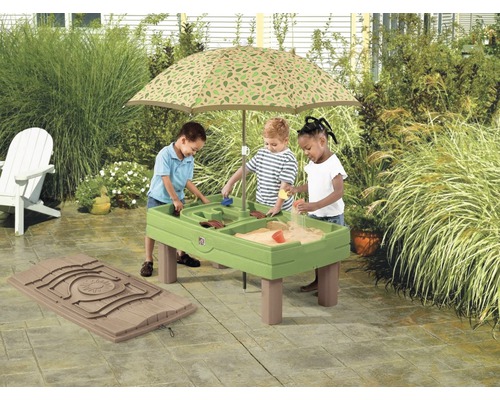 Drie kinderen spelen aan een groene zand- en watertafel met parasol in de tuin.