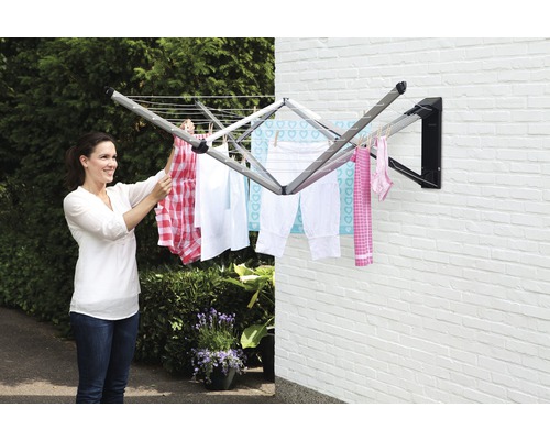 Vrouw hangt wasgoed op aan een wanddroogrek in de tuin.