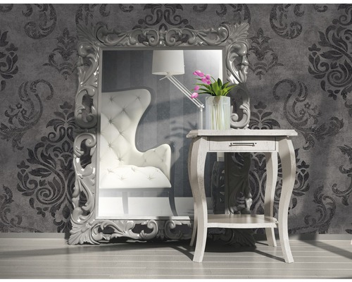 Decoratieve kamer met grote spiegel, fauteuil en bijzettafel voor een behangen muur.