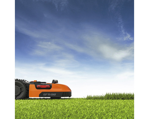 Oranje robotmaaier op gazon tegen blauwe lucht