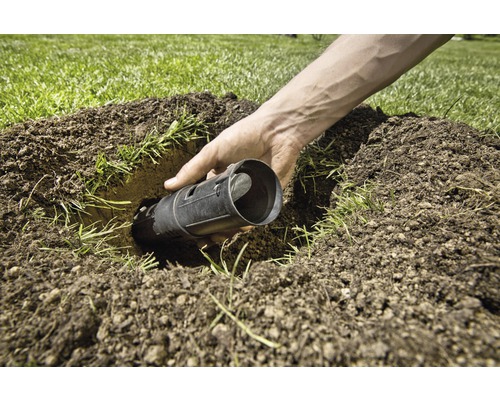 Een persoon plaatst een mollenval in een gat in het gazon.