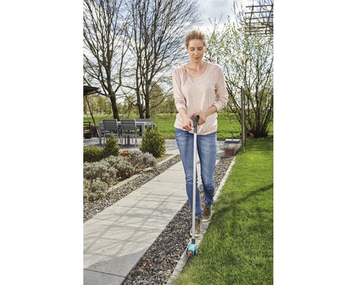 Vrouw gebruikt een graskantensnijder in de tuin om graskanten te knippen.