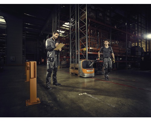 Twee arbeiders in een magazijn met stellingen en vorkheftruck. Een maakt aantekeningen.