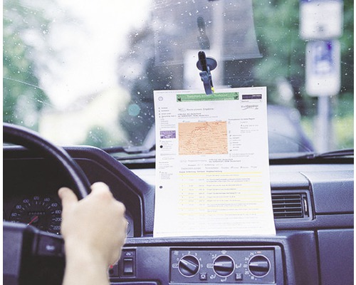 Een vel papier met informatie, bevestigd met een zuignaphouder aan de voorruit van een auto.