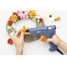 Persoon lijmt bloemen op een krans met een lijmpistool