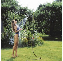 Vrouw onder een tuindouche in de tuin.